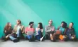 "Pairs of people talking and sitting in front of a teal wall"